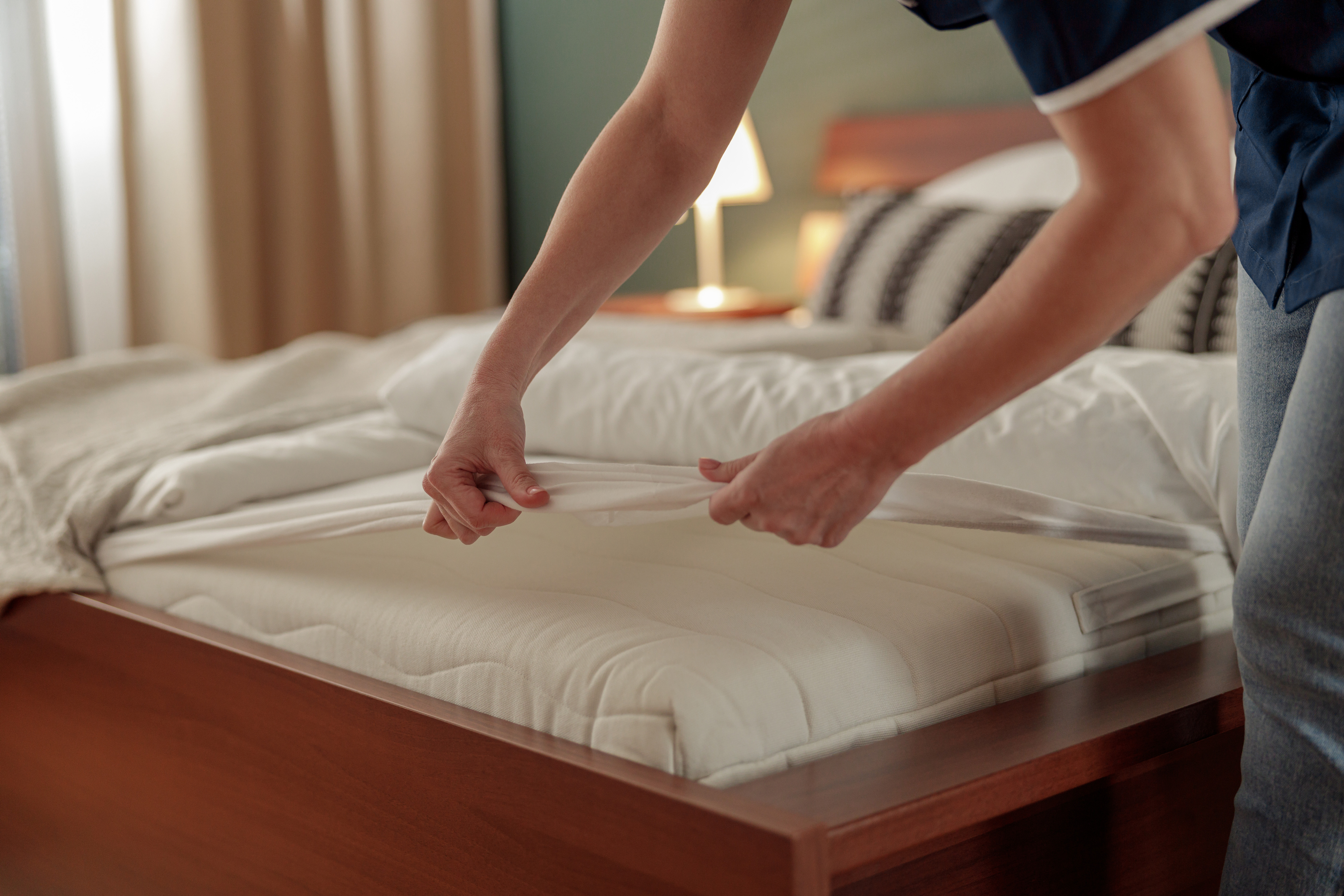 A person putting a white sheet over their mattress