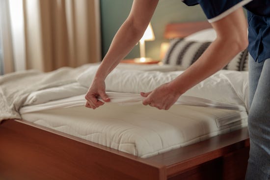 A person putting a white sheet over their mattress