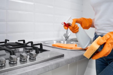 Mulher segurando um frasco de detergente em spray e uma esponja para limpar um fogão de cozinha.