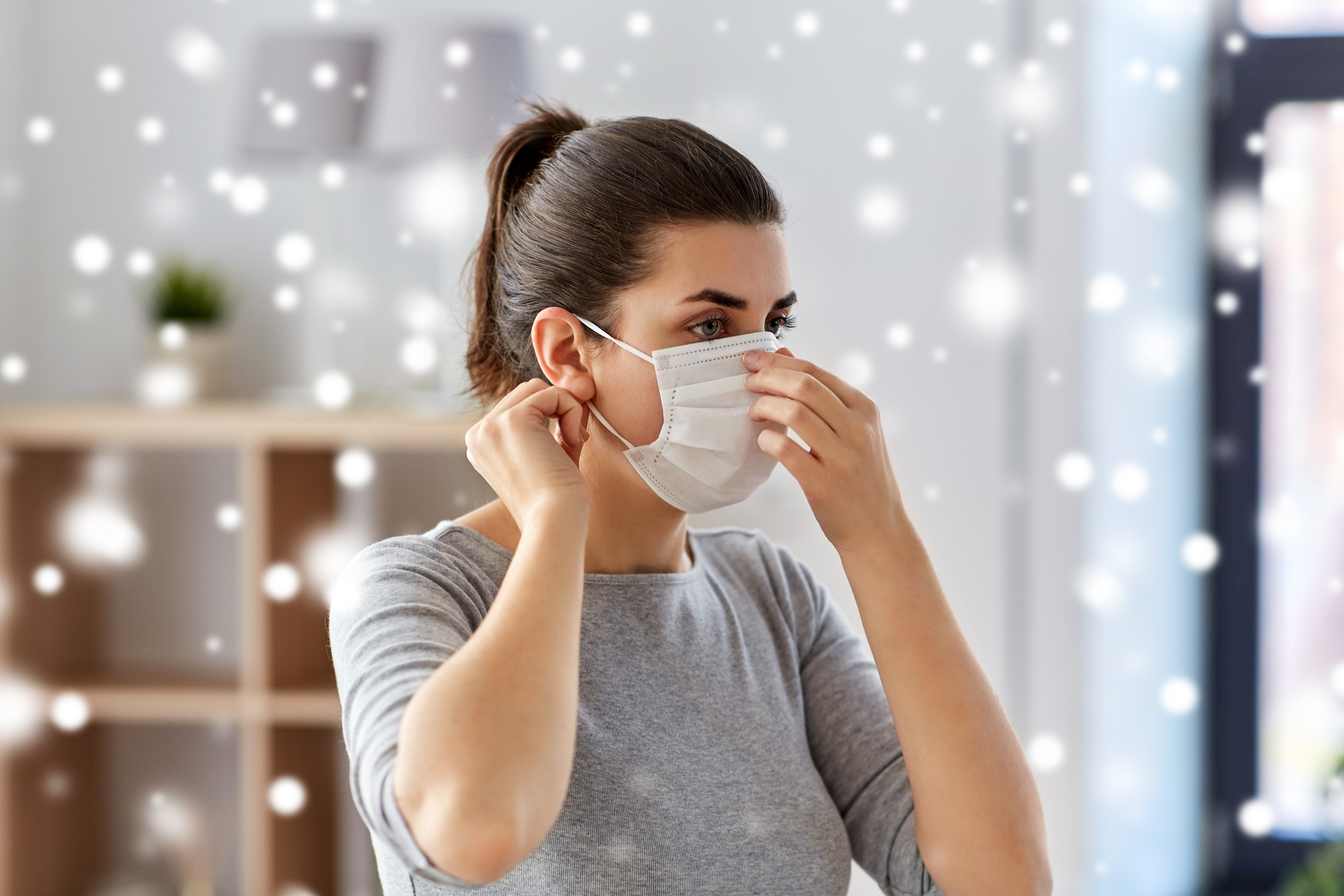 A woman putting on a protective face mask indoors.