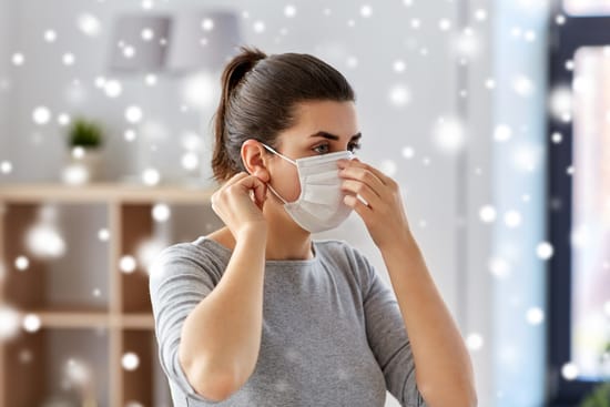 A woman putting on a protective face mask indoors.