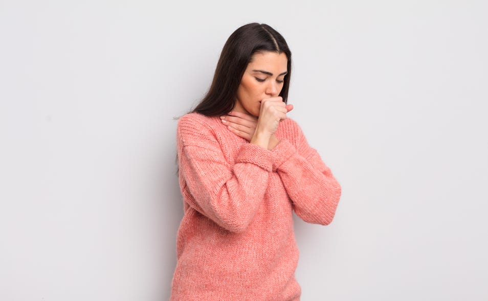 Woman covering her mouth while coughing and other hand placed on her throat