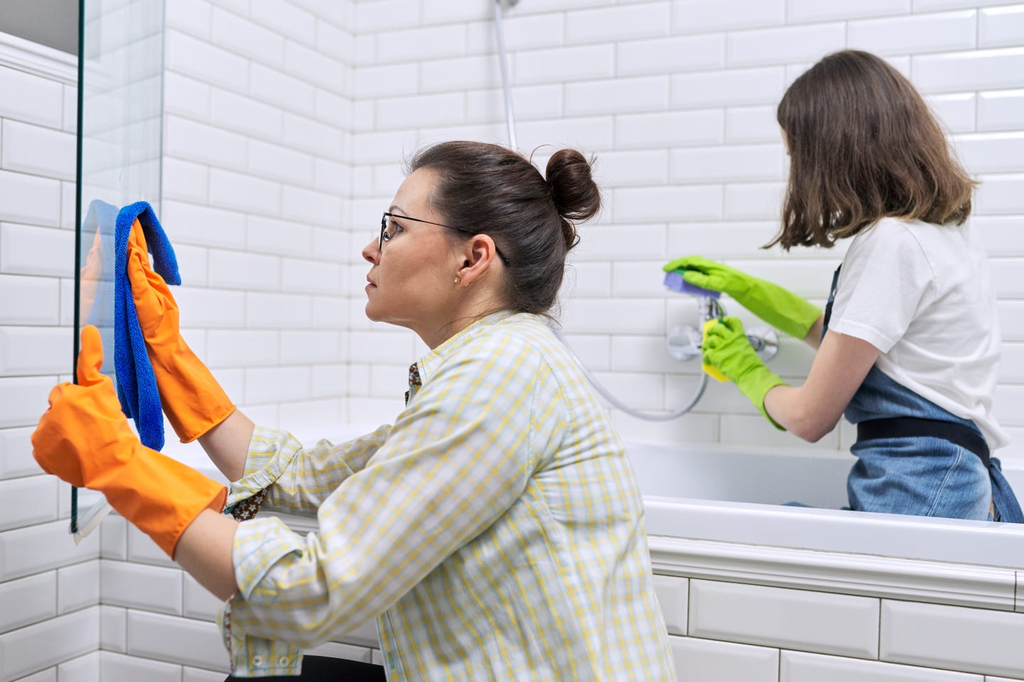Two women cleaning shower bathtub glass wall and shower faucet