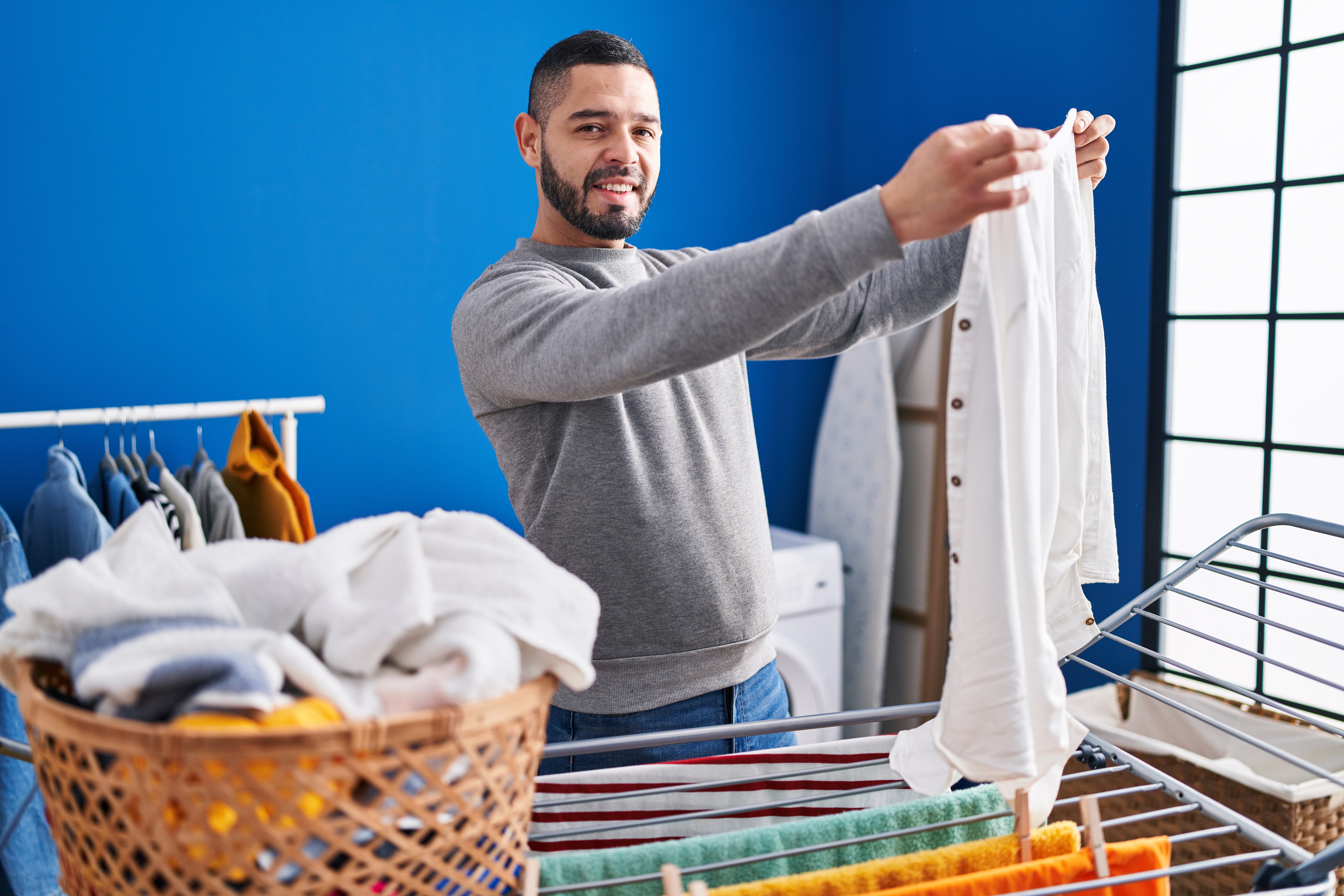 Man holding white shirt near drying rack.