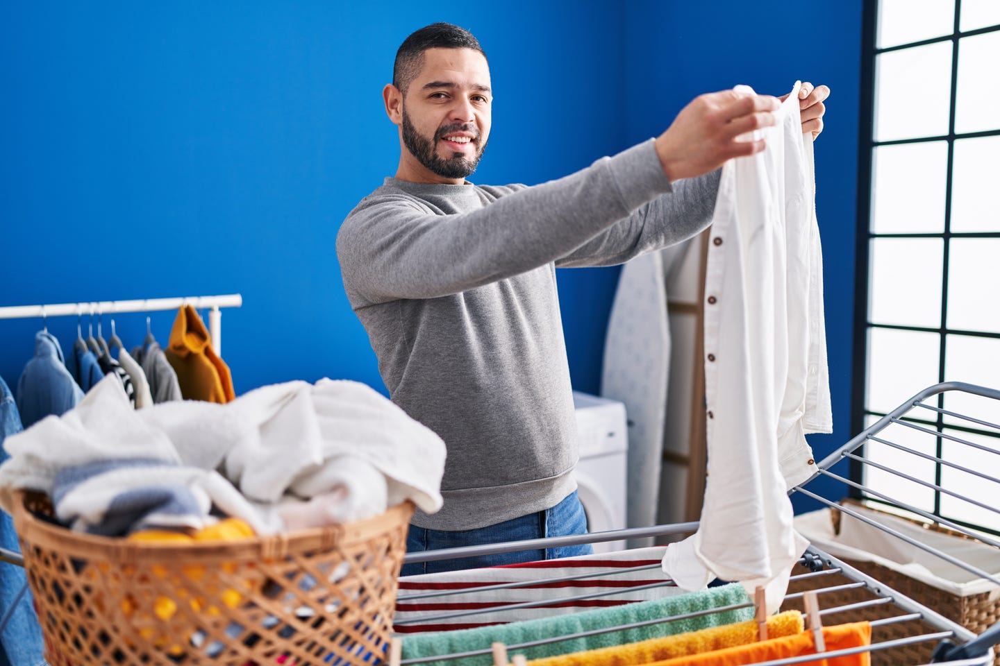Man holding white shirt near drying rack.