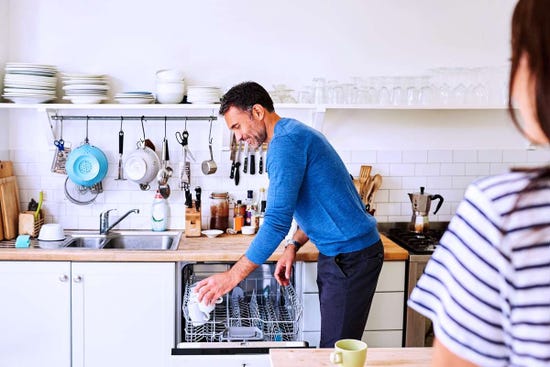 Man putting dirty coffee mugs into dishwasher in kitchen