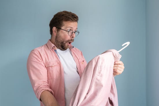 A man with a shocked expression staring at a shirt on a hanger