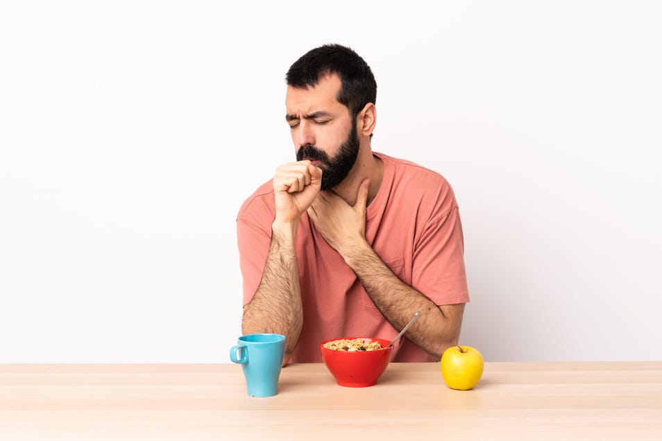 Man coughing into his hand while eating a meal