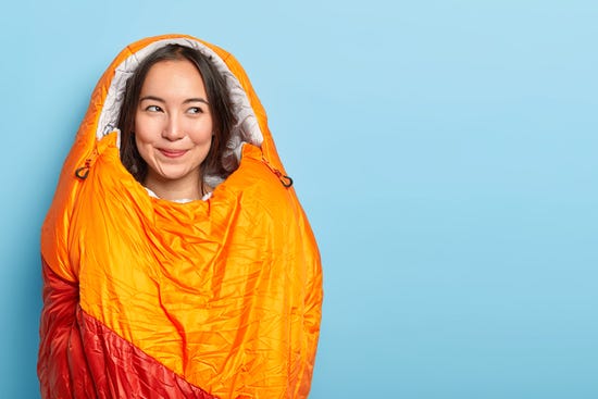 Woman inside of orange sleeping bag with blue background