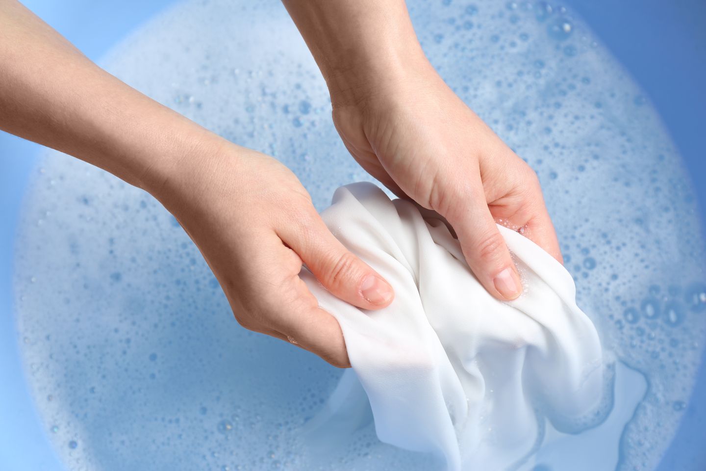Person handwashing a white clothing item in a blue tub