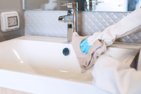 Hands wearing rubber gloves cleaning the sink with a microfiber cloth in the bathroom