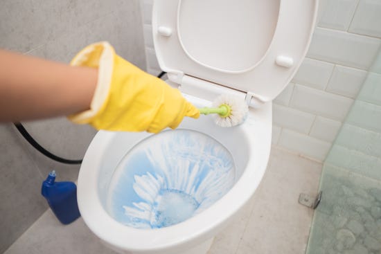 A person wearing a rubber glove is cleaning the toilet with a toilet brush
