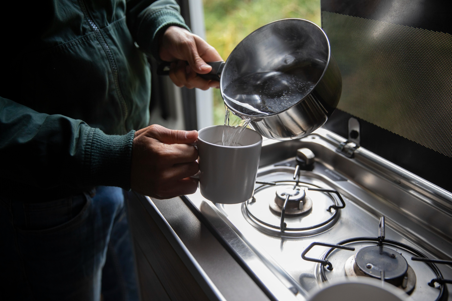  Pessoa despejando água quente de uma panela em uma caneca sobre fogão. 