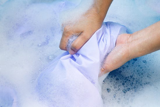 Top view of a person’s hand washing a jersey in soapy water.