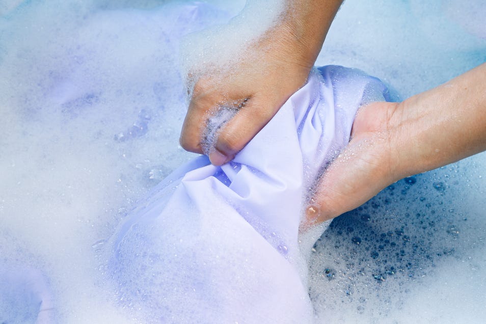 Top view of a person’s hand washing a jersey in soapy water.