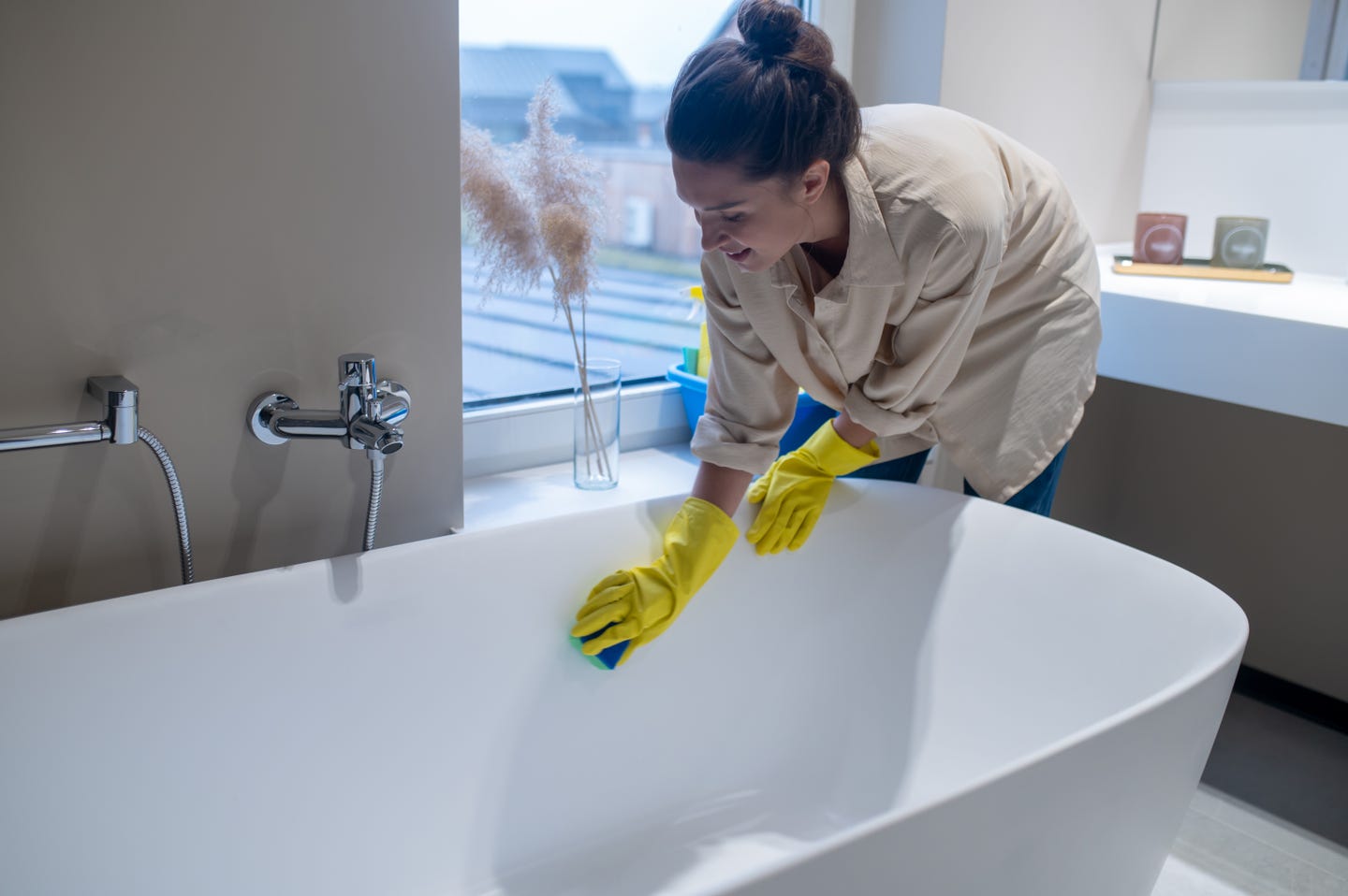 A woman wearing gloves cleaning a bathtub with a sponge