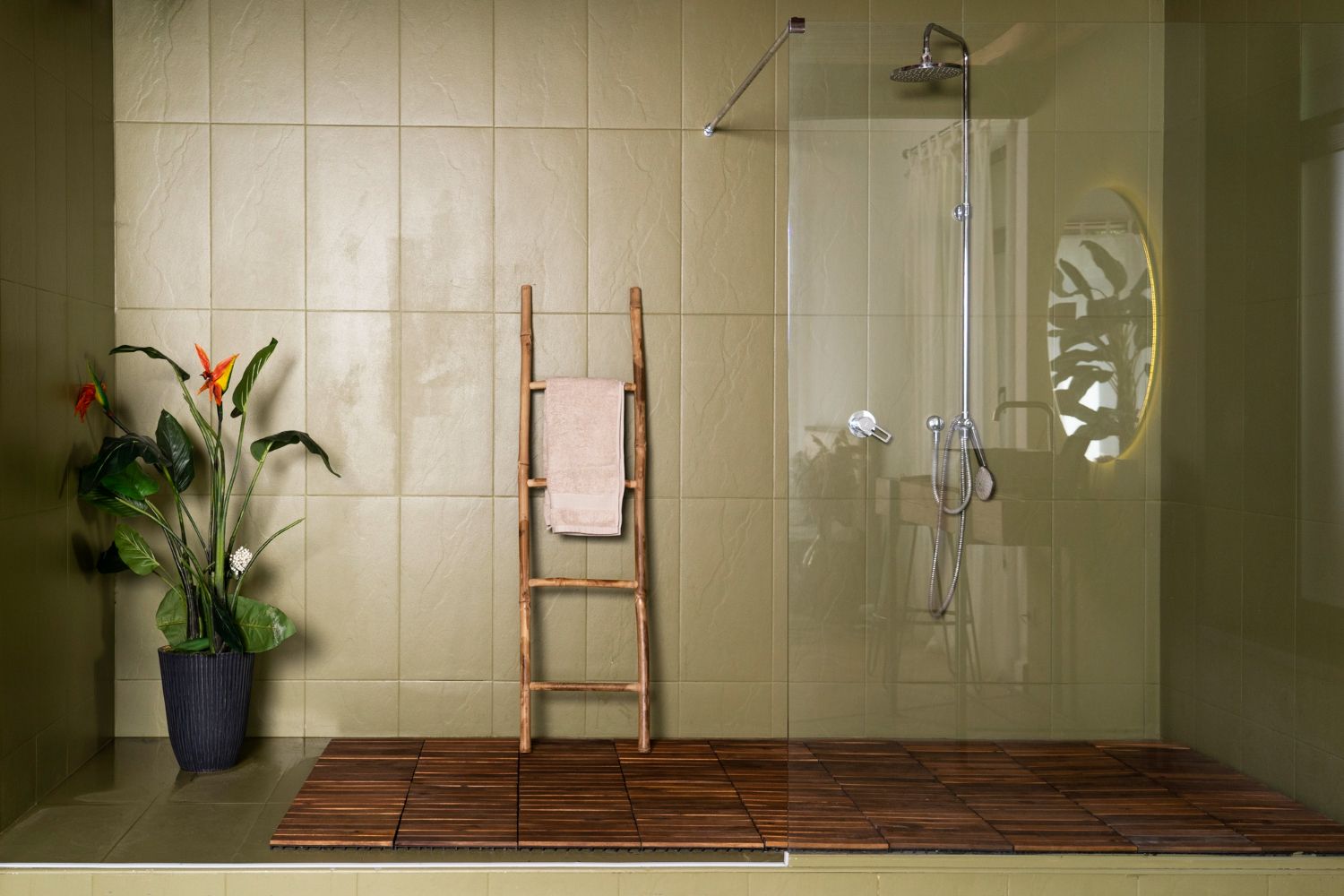 Ambiente de banheiro minimalista com plantas, toalhas e piso de madeira, com box de vidro no chuveiro.