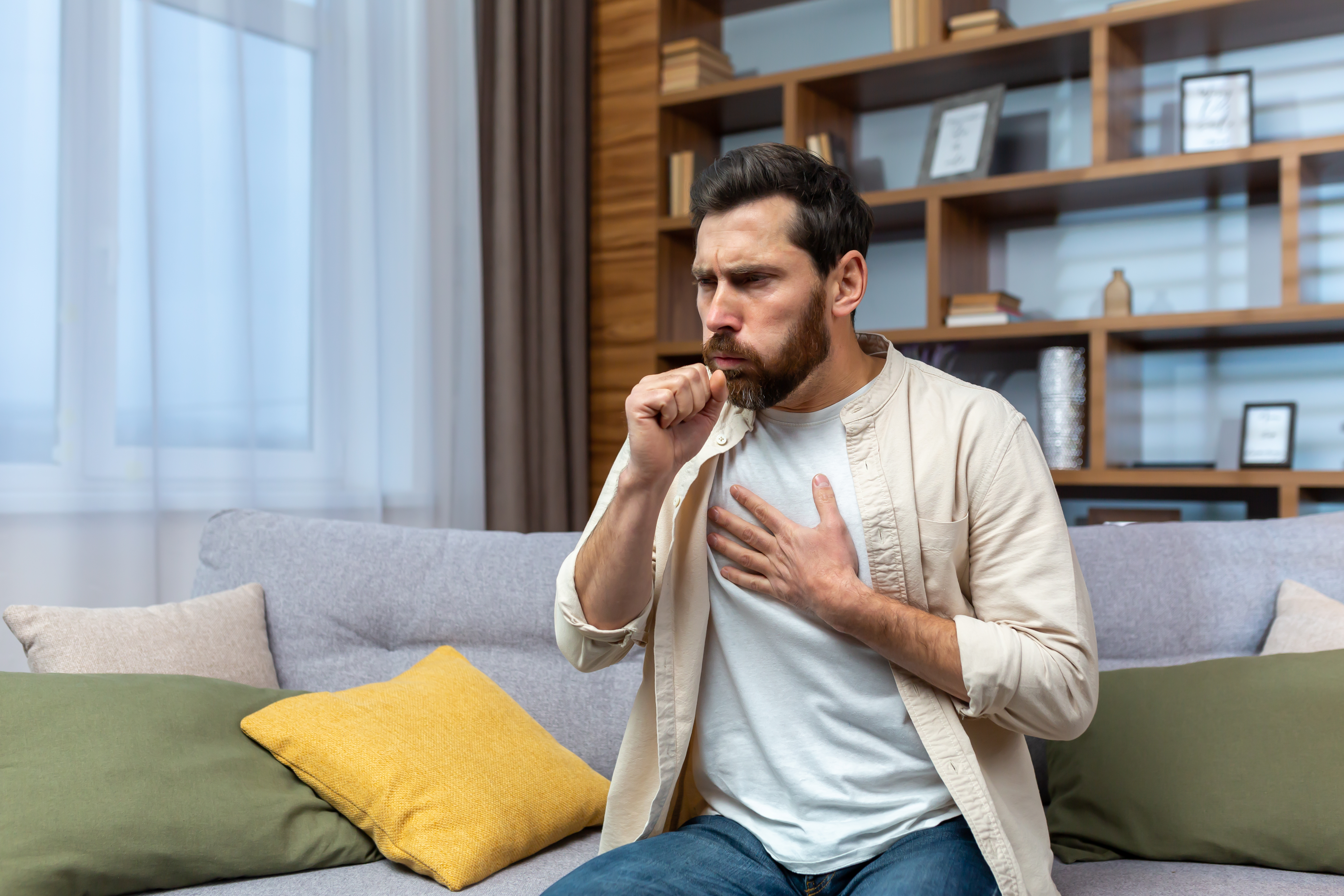 A man holding his chest with his hand while holding his hand in front of his mouth.