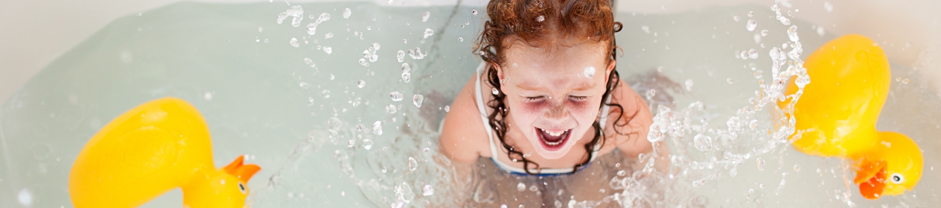 A baby girl is playing and bathing in tub with rubber ducks
