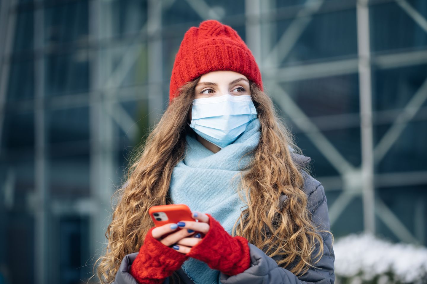 Woman in a red hat and face mask holding a smartphone