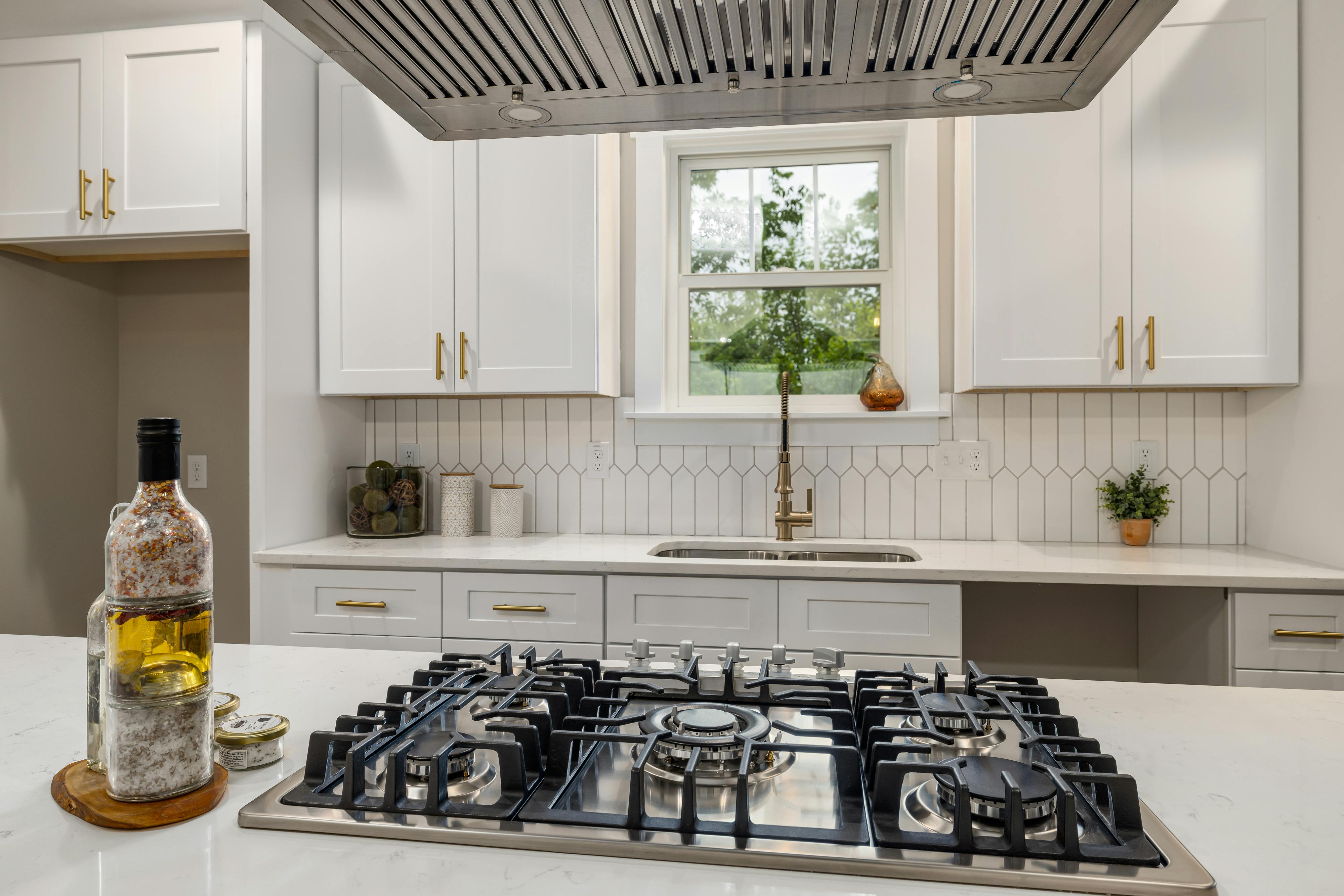 Vista de uma cozinha moderna com um cooktop em primeiro plano, com uma janela com vista externa ao fundo.