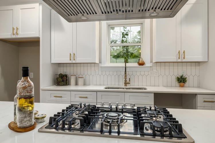 Vista de uma cozinha moderna com um cooktop em primeiro plano, com uma janela com vista externa ao fundo.
