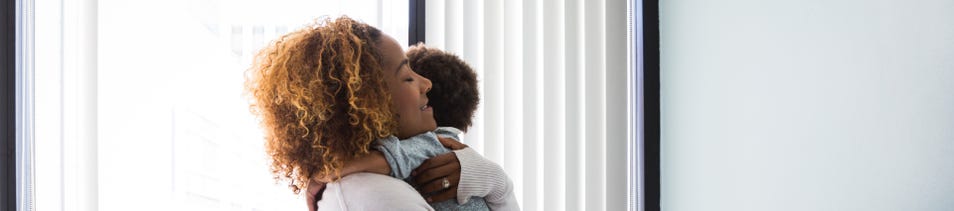 Woman holding and embracing a child in a bright white room