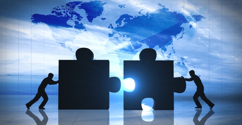 business merger and acquisition concept, image shows two jigsaw puzzle pieces joining with world map in the background.