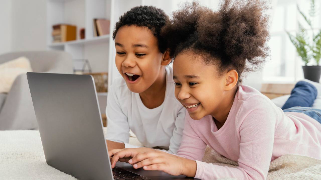 Side view of two siblings at home together playing on laptop.