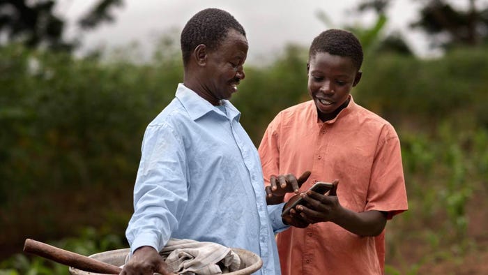 A young man helps an African farmer use a smartphone in an agricultural field. A young man helps an African farmer use a smartphone in an agricultural field.