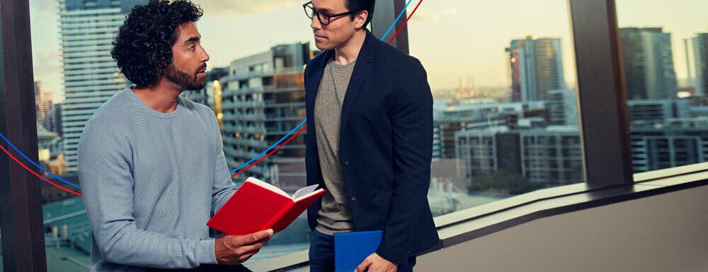 Two traders have a conversation while looking at a book