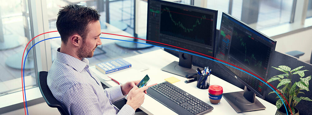 Man sits in front of two screens and trade on his mobile phone