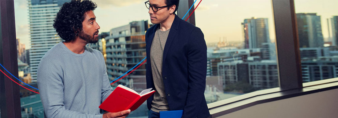 Two men have a conversation while looking at a book