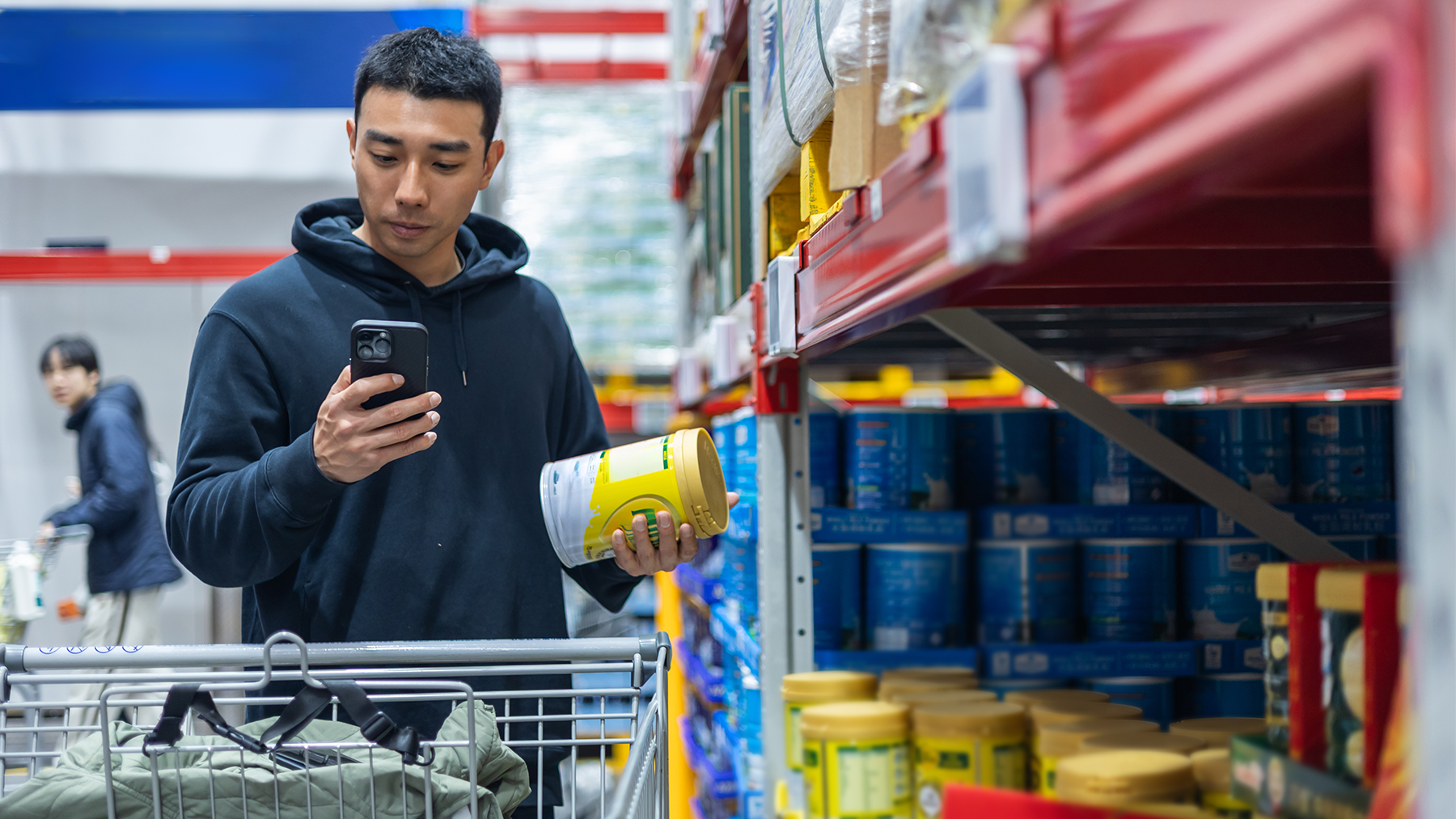 A young Asian man in a supermarket uses a mobile phone to check the ingredients list of a product