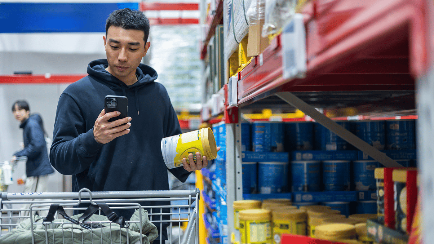 A young Asian man in a supermarket uses a mobile phone to check the ingredients list of a product A young Asian man in a supermarket uses a mobile phone to check the ingredients list of a product
