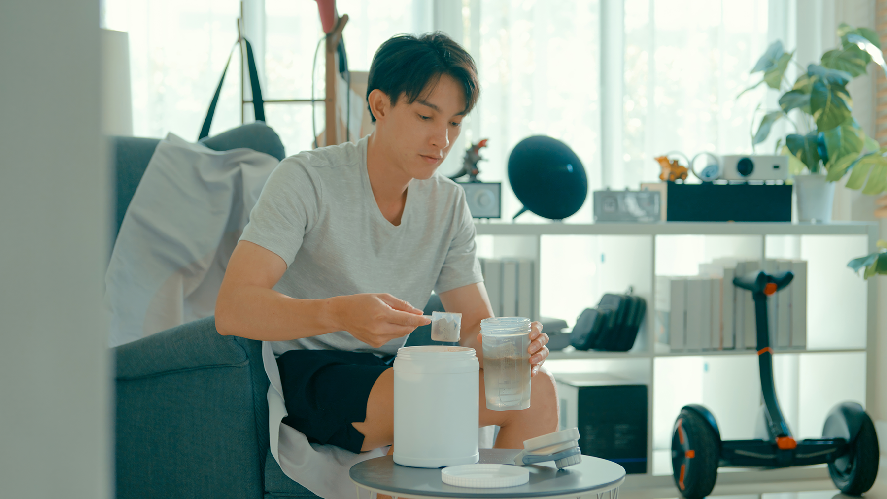 Young Asian man preparing protein shake on sofa in living room at modern home