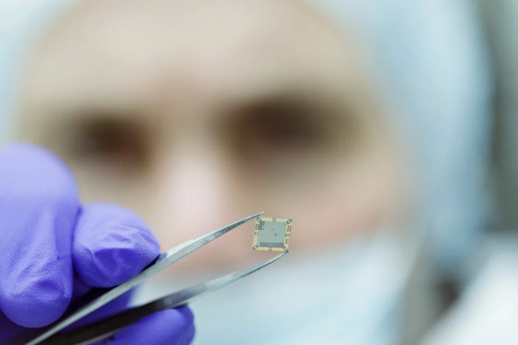 A scientist in protective lab hear holds a chip between tweezers