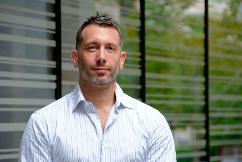 A photo of Q-CTRL founder and CEO Michael Biercuk standing in front of window blinds
