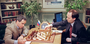 Garry Kasparov studies a chessboard as a computer operator checks moves on a computer monitor.