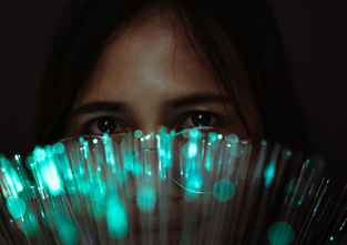 A woman in glasses looks over a bundle of lit optic fibers