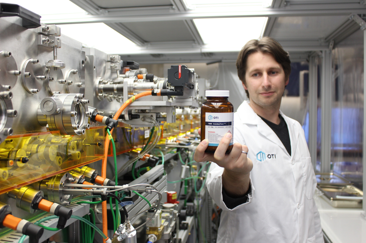 Scott Genin wearing a lab coat holds a jar of chemicals in a laboratory Scott Genin wearing a lab coat holds a jar of chemicals in a laboratory