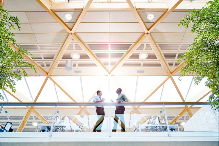 Two office workers talk on an elevated platform in a glass-sided office. 