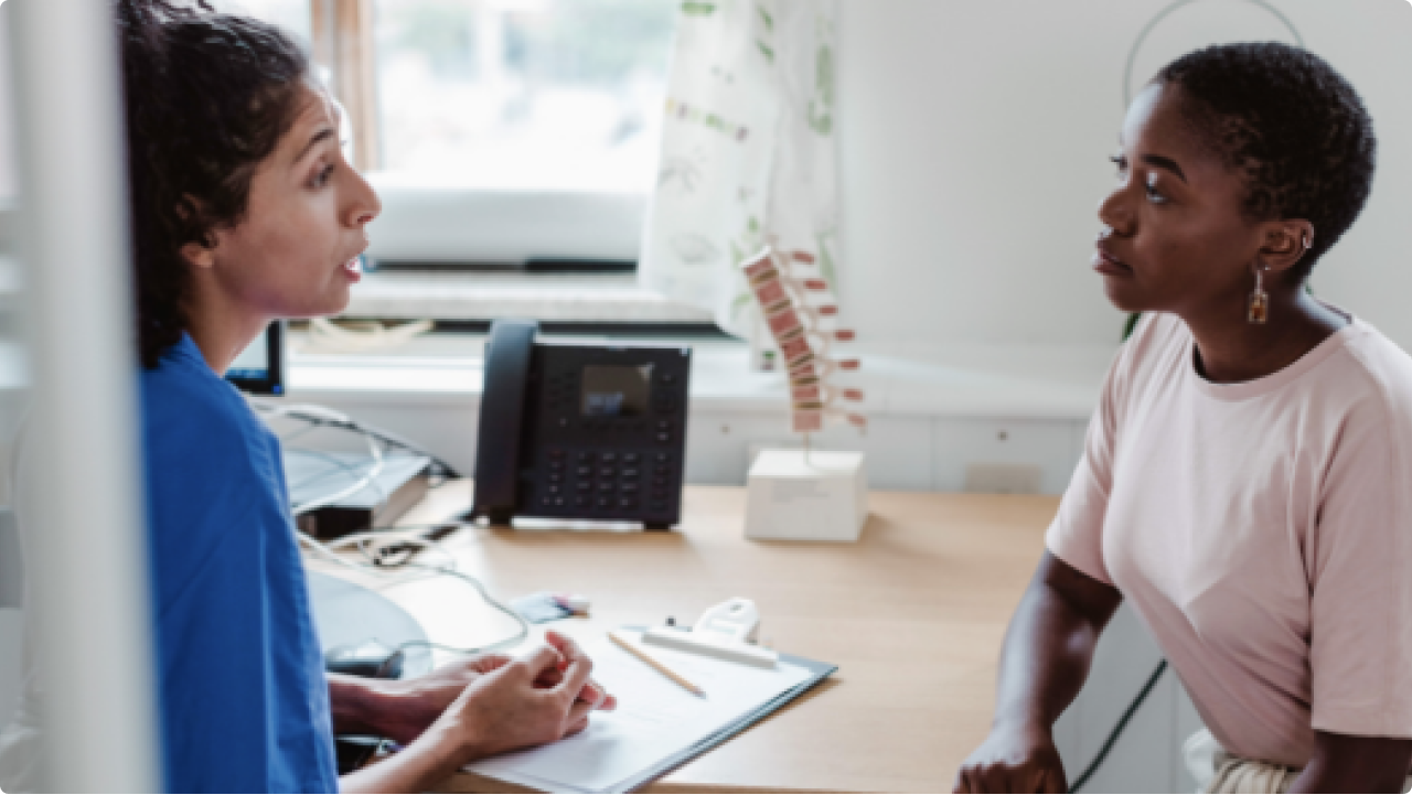 Image of a female healthcare professional sitting at a desk with a female patient