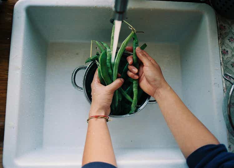 Hands cleaning vegetables in kitchen sink.