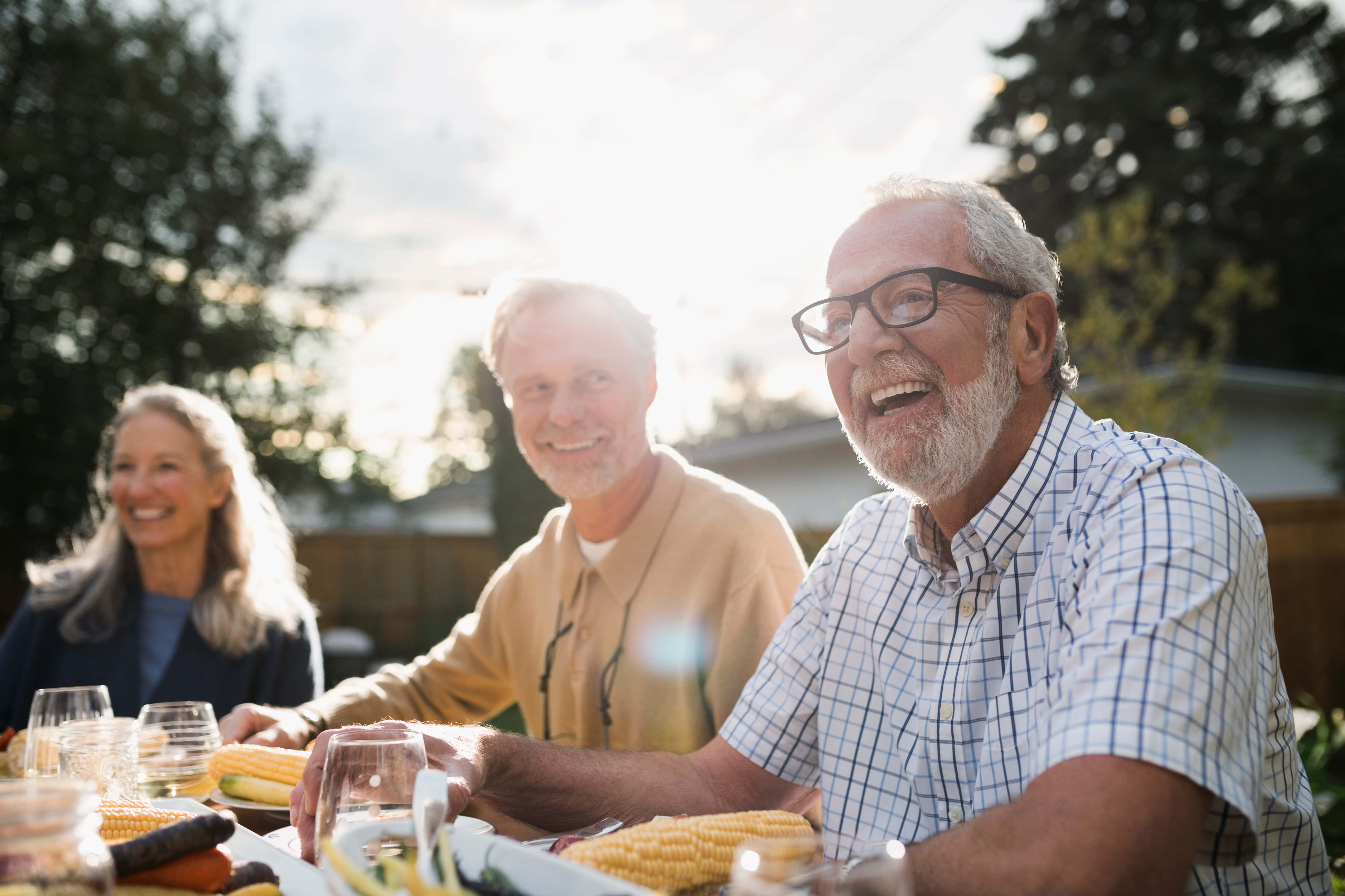 2 older man sitting outdoors at a table and laughing