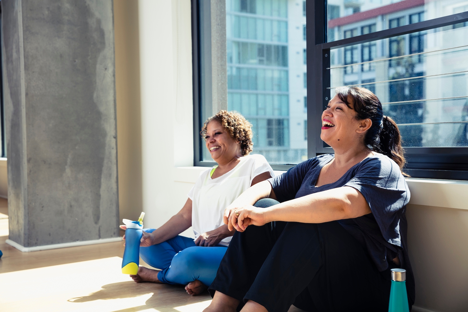2 ladies sitting on the ground against a window 