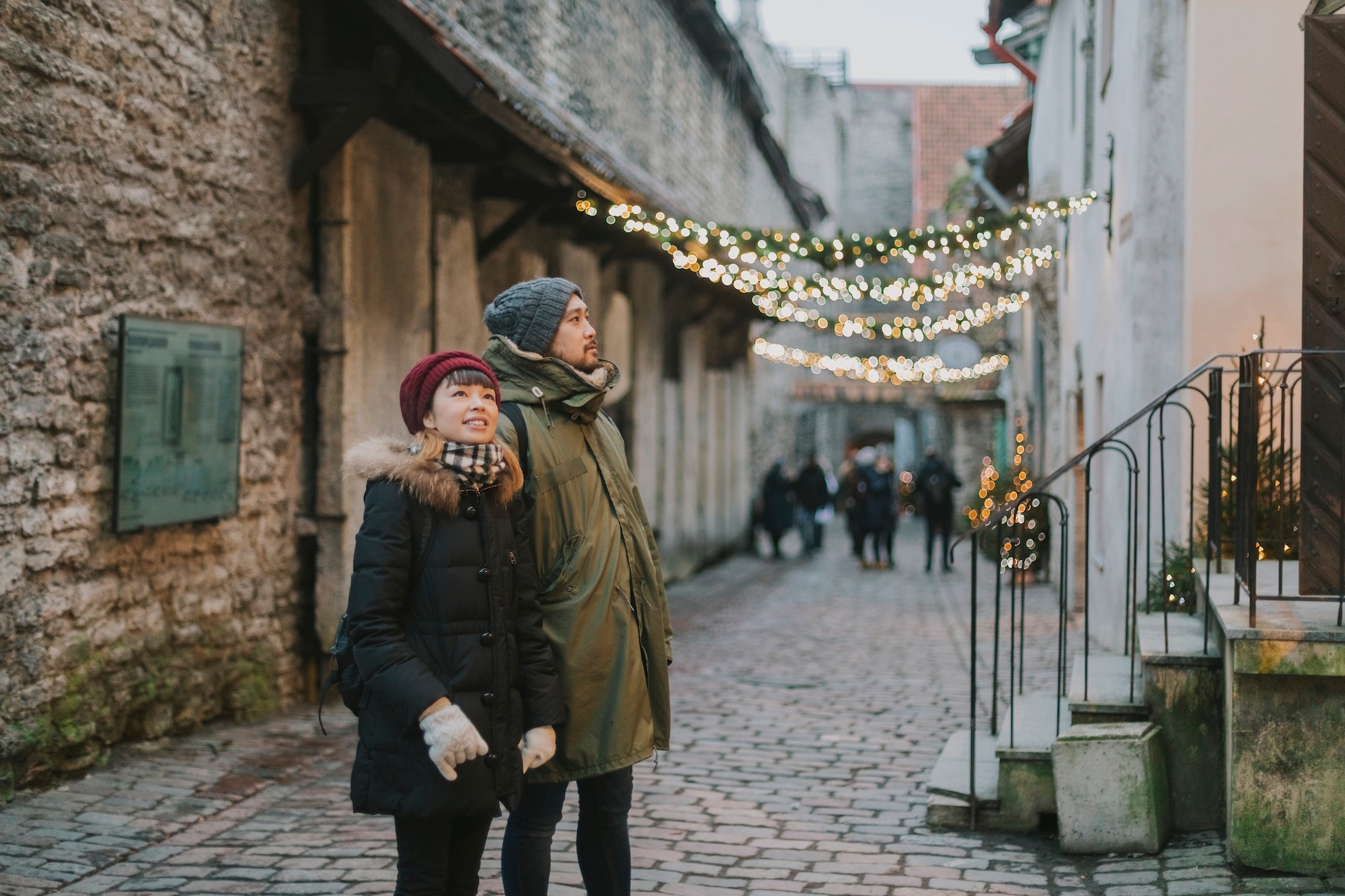 A couple strolls in a town with colorful Christmas lights