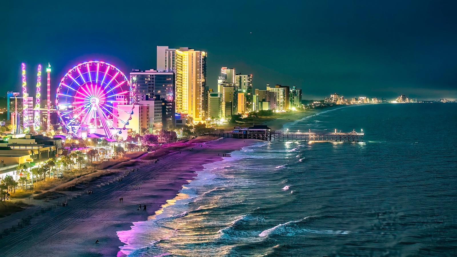 Night view of Downtown Myrtle Beach skyline featuring a ferris wheel and beach, illuminated against the dark sky