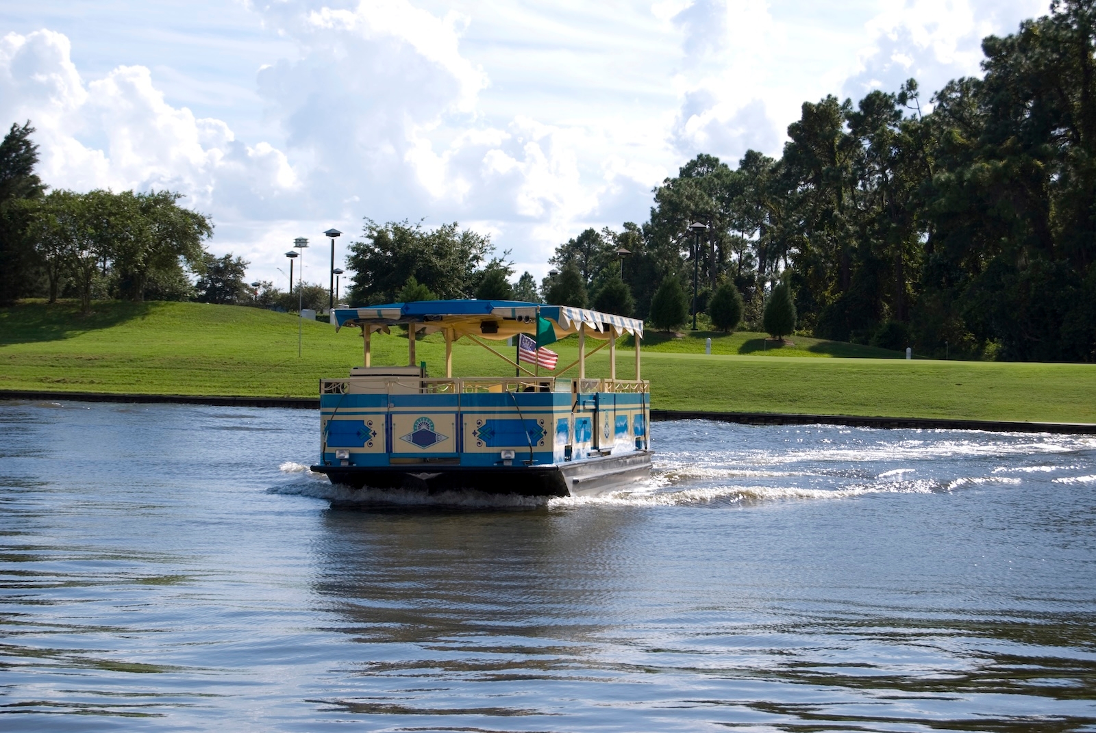 A Disney World boat glides across the water, surrounded by lush greenery and a clear blue sky