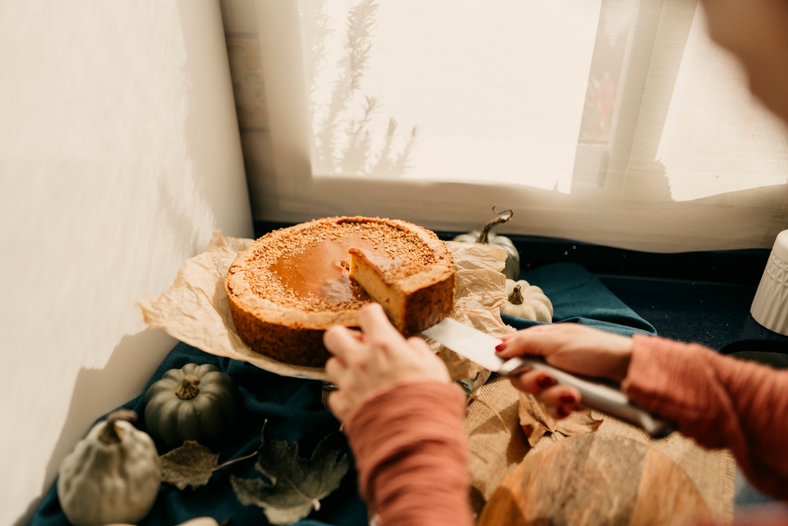 A person cutting a pumpkin pie on a table during a Friendsgiving celebration, after a cooking competition